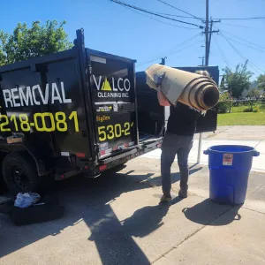Valco crew member loading a rolled carpet into the branded dump trailer